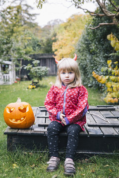 Little girl with red horns in garden at Halloween
