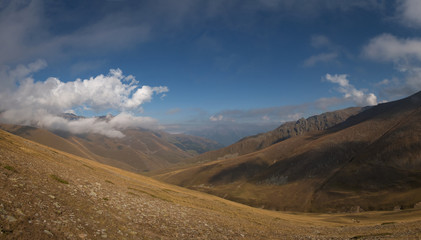 wide mountain gorge in autumn with deep blue sky and white clouds