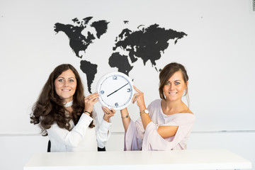 Two young girls twins with clock on the background of the world map