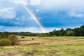 autumn landscape with cloudy weather, large rainy clouds over a chamfered yellow field, the rainbow is in the sky