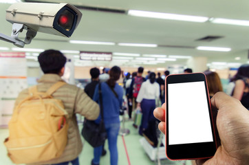 hand holding mobile smart phone and CCTV security indoor camera system operating with blurred image of people queue at immigration control at airport,