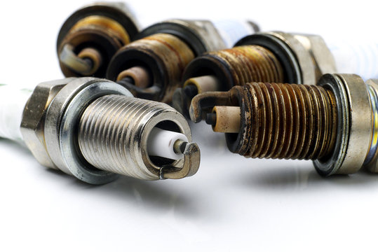 one brand new spark plug in front of four used ones on white background, macro