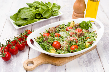 Meatballs and spinach oven dish with cherry tomatoes, potatoes and herbal cheese and cream sauce. One pot meal on White wood background.