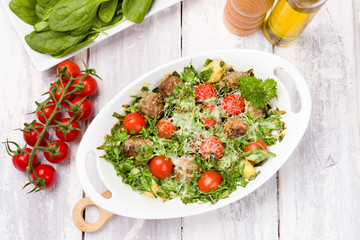 Top View of meatballs and spinach oven dish with cherry tomatoes, potatoes and herbal cheese and cream sauce. One pot meal on White wood background.