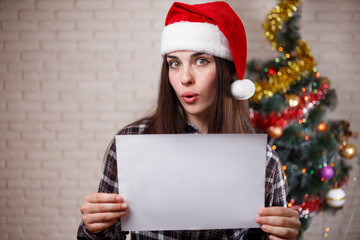 Young beautiful women in Santa cap with empty sheet of paper in hands. Free space for advertisement...