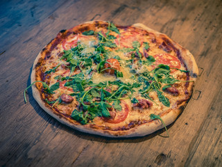 Italian pizza with ruccola or arugula and truffle sausage or salsiccia. On wood background.