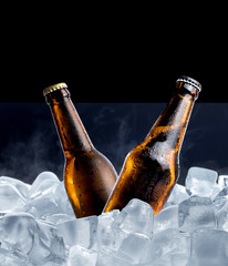 Cold bottle of beer with drops in ice cubes isolated on black background