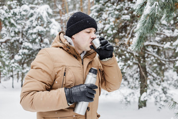 man with hot drink in thermos cup in winter forest