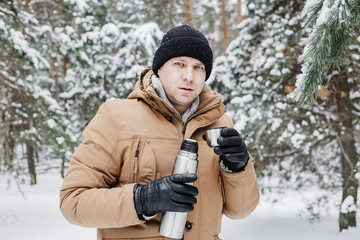 man with hot drink in thermos cup in winter forest