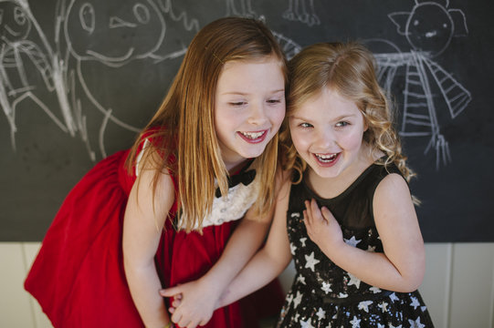 Two young girls dressed up in their holiday best hold hands laughing.