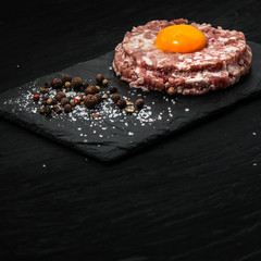 meat cutlet raw (minced) with raw egg, a mixture of peppers, peas and salt on a slate plate - tartar
