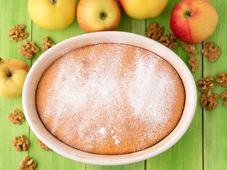 ready Apple pie biscuit dough on a green wooden background with apples and nuts. Charlotte dusted...