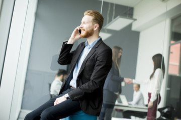 Businessman with ginger hair using mobile phone while other business people working in office