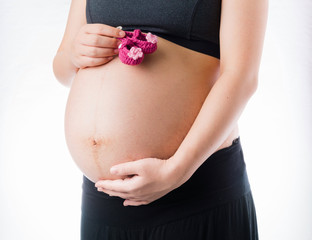 Happy pregnant woman take pink wool baby shoes in hand and touch belly, isolated on white background