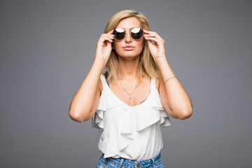 Young attractive lady in jeans and sunglasses posing in studio on grey background not isolated, blond girl hipster summer outfit concept, photo with place for text