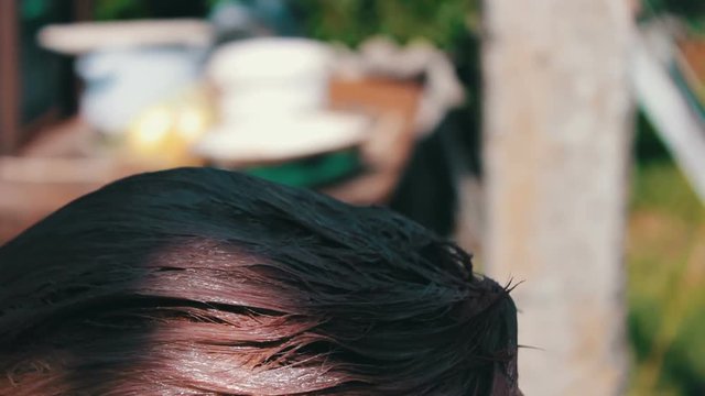 Woman paints her hair with brown paint in the summer on the street. Hair coloring at home