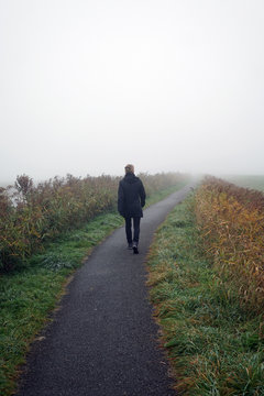 Woman walking on path on foggy day in autumn