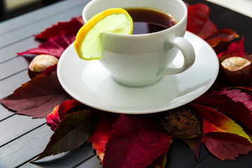 Cup of tea with lemon. A cup of tea lies on a ground with boards and red leaves. Lemon in a cup. High key. Warm tea in cool autumn days.