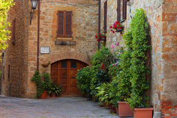 Obraz na płótnie Canvas Beautiful narrow street with sunlight and flowers in the small magical and old village of Pienza, Val D'Orcia Tuscany, Italy.