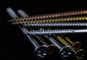 unterschiedliche Kreuzschrauben aus Messing und Edelstahl auf schwarzem Hindergrund, Schrauben mit...