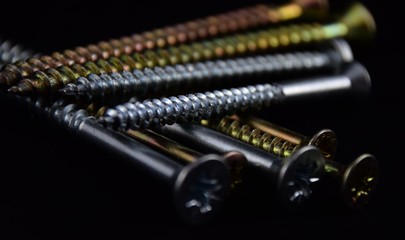 unterschiedliche Kreuzschrauben aus Messing und Edelstahl auf schwarzem Hindergrund, Schrauben mit...