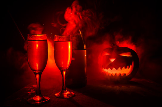 Two glasses of wine and bottle with Halloween - old jack-o-lantern on dark toned foggy background. Scary Halloween pumpkin. Useful as party poster
