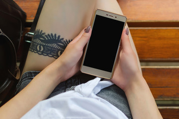 young woman using smartphone while sitting on the bench with the tattoo on the leg