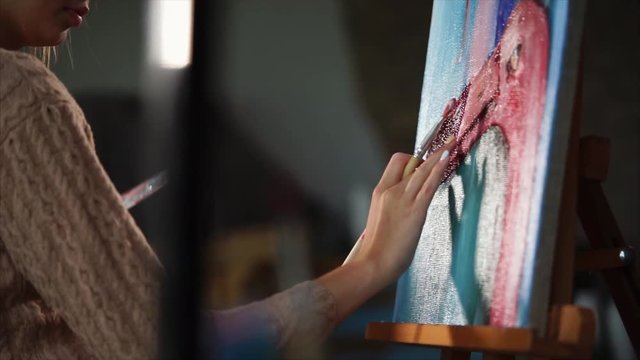 Close up shot of the process of creating a picture, a woman paints with her hands and oil paints a pink flamingo, the picture stands on an easel