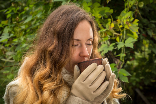 Dreaming girl in warm clothes on autumn park testing a hot bever