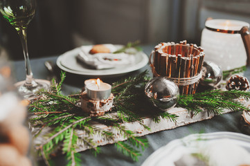 Festive Christmas and New Year table setting in scandinavian style with rustic handmade details in natural and white tones. Dining place decorated with pine cones, branches and candles