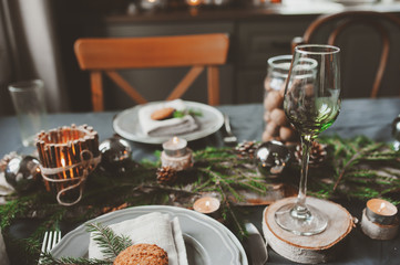 Festive Christmas and New Year table setting in scandinavian style with rustic handmade details in natural and white tones. Dining place decorated with pine cones, branches and candles