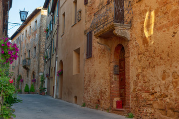 Beautiful narrow street with sunlight and flowers in the small magical and old village of Pienza, Val D'Orcia Tuscany, Italy.