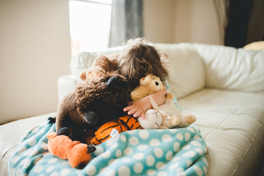 Little girl hiding in her pile of stuffed animals