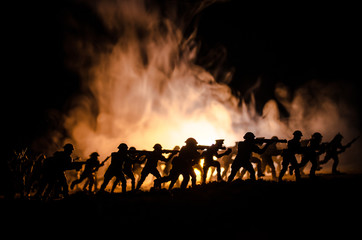 Fototapeta na wymiar Military silhouettes of soldiers against the backdrop of dark foggy sky. Battle scene with explosion and burning clouds behind fighing soldiers. Toy decoration