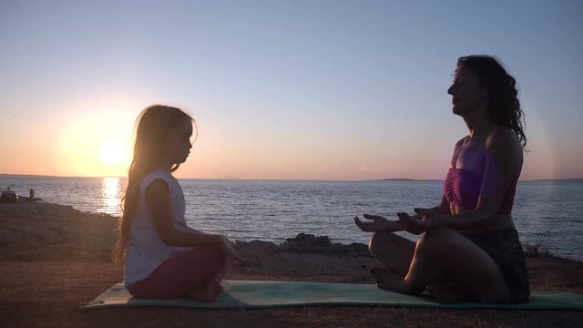 Mother And Child Meditating At Sunset By The Sea. 