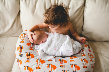 Little toddler girl holding her newborn brother