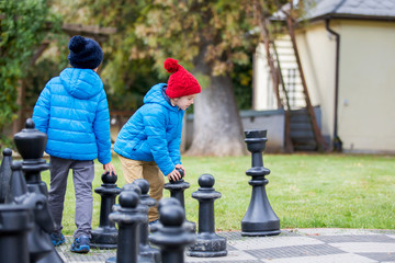 Two children, boy brothers, playing chess with huge figures in the park