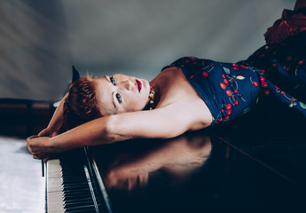 Woman in cherry dress lying on the piano