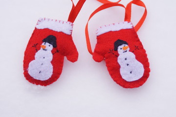 red felt santa mittens with white snowman and ribbon on the snow