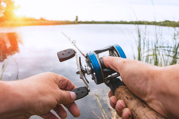 A man is fishing with a backcasting reel. Hands, a rod and a backcasting reel in the background of...