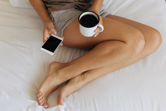 Woman in the bed reading smartphone and drinking coffee