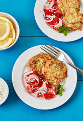 Zucchini fritters, vegetarian zucchini pancakes, served with fresh tomato and red onion salad and yogurt sauce, top view. Healthy, vegetarian food