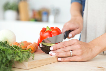 Hands of young woman cutting fresh vegatebles in the kitchen.