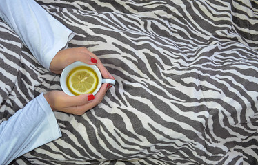 Ill young woman is holding cup of tea on the bed