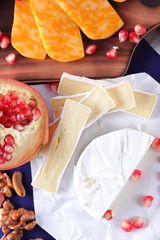 Camembert cheese, marbled cheese, different cheeses, dark blue grapes, red pomegranate, green grapes, peanuts and walnuts on a wooden board with an empty place for writing