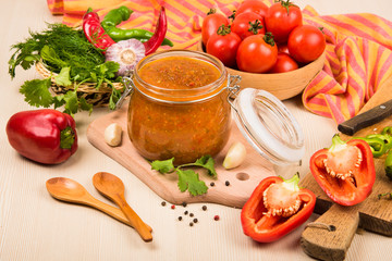Tomato sauce (ketchup, adzhika) and vegetables on a beige table. Home preservation.
