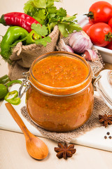 Tomato sauce (ketchup, adzhika) and vegetables on a beige table. Home preservation.