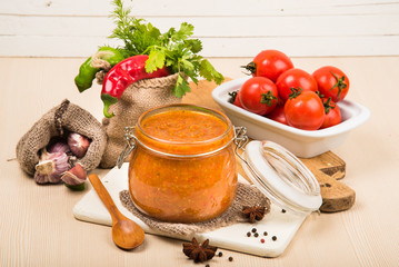 Tomato sauce (ketchup, adzhika) and vegetables on a beige table. Home preservation.