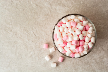 White and pink mini marshmallows in glass bowl on stone background.