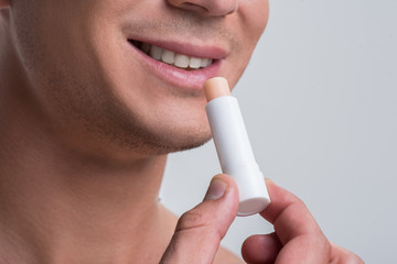 Cheerful naked man is using cosmetic balm